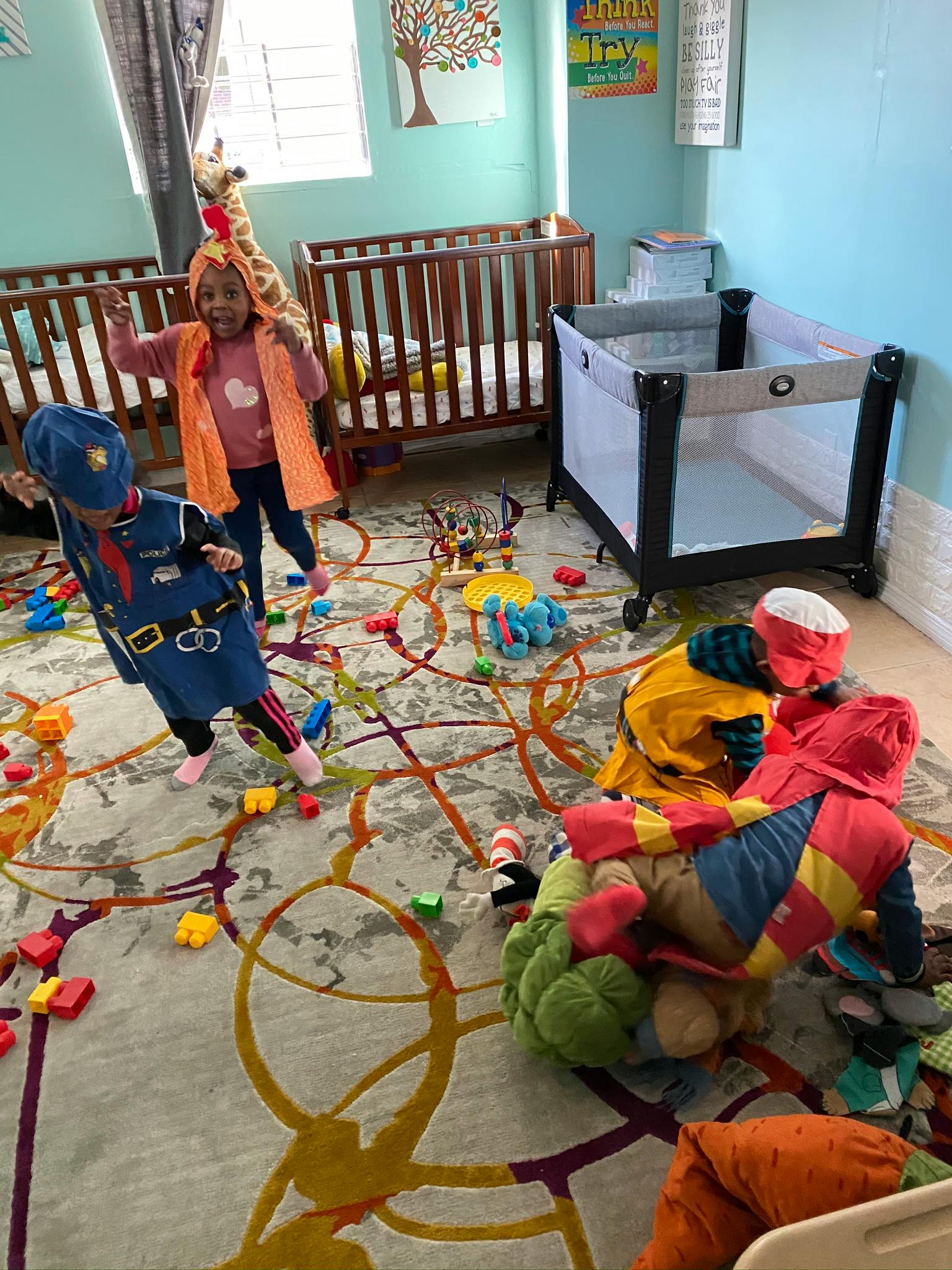 Three children playing on a rug with toys, two cribs in the background