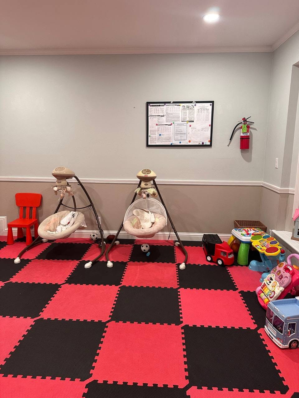 Two baby swings on a red and black checkered floor in a room with toys