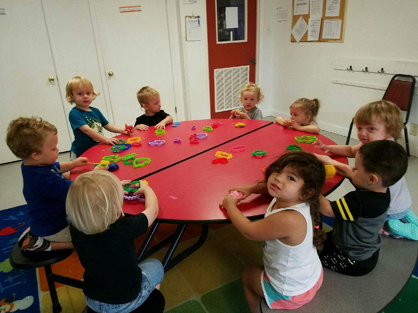 Children playing with toys at a red table in a classroom