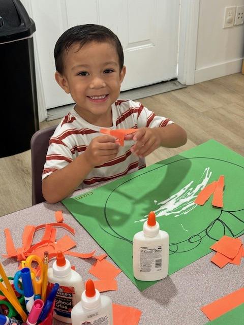 Child crafting with orange paper and glue at a table