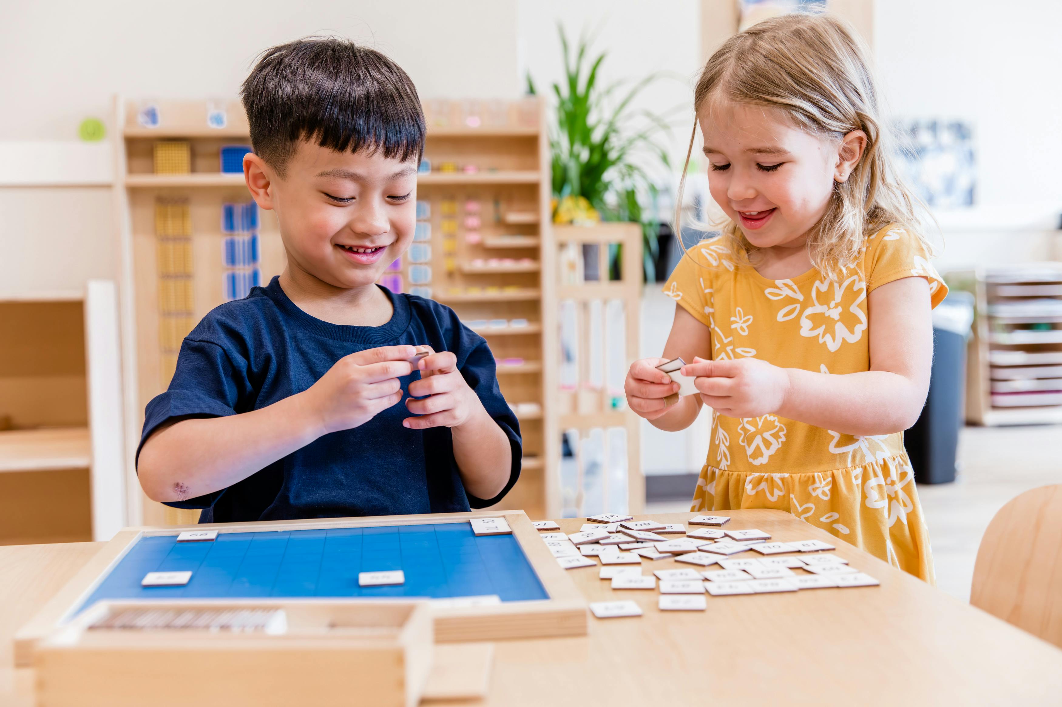 Two children playing with puzzle pieces at a table in a classroom