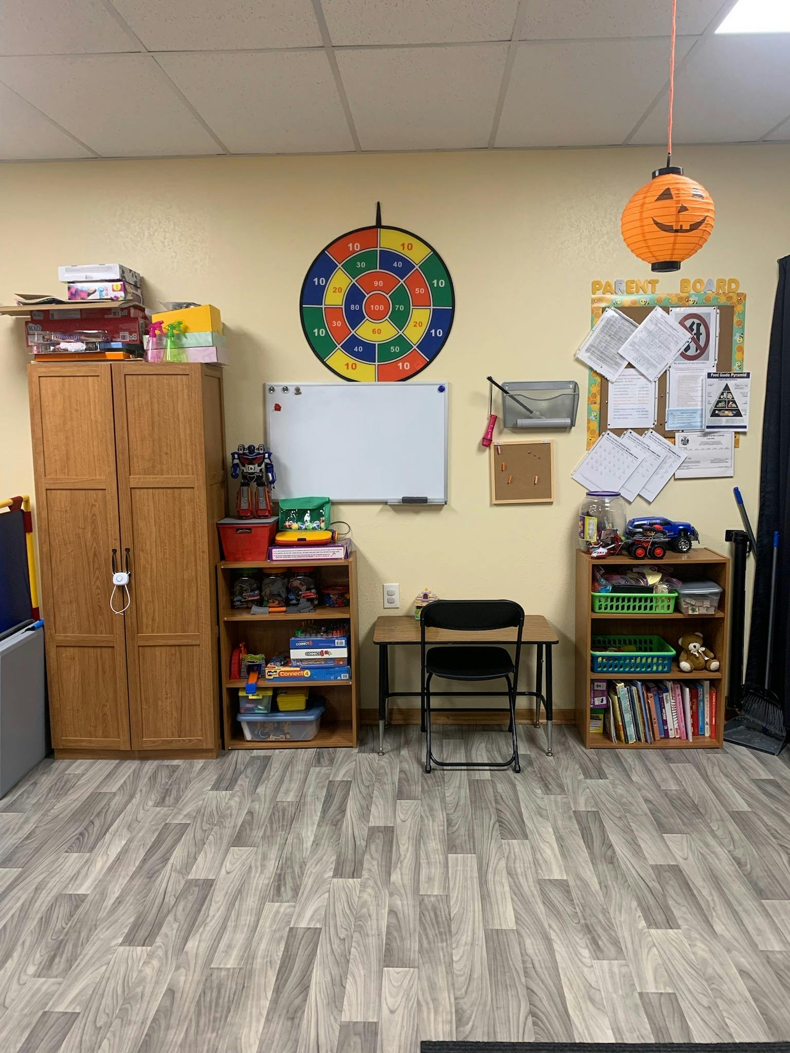 Room with a colorful dartboard, whiteboard, desk, chair, and shelves