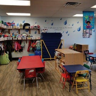 Classroom with small tables and chairs, shelves with toys and clothes