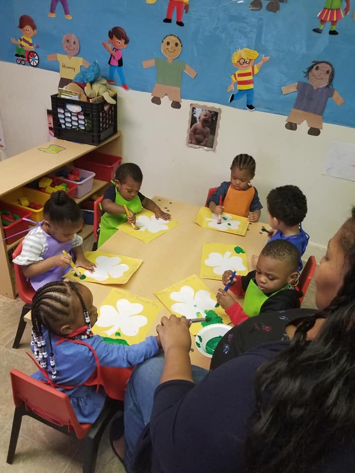 Children painting shamrocks at a table in a classroom