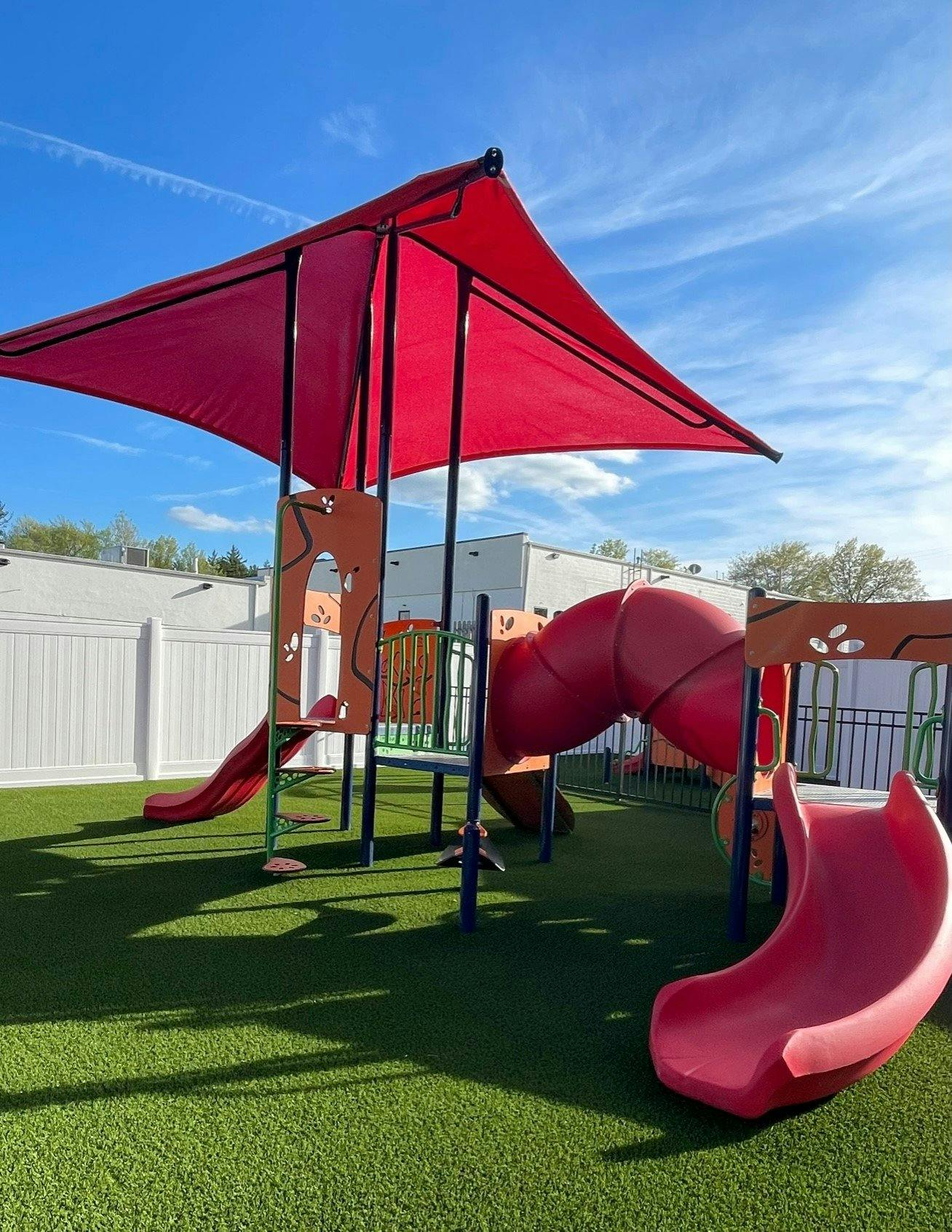 Playground with red slides and a red shade canopy overhanging shade