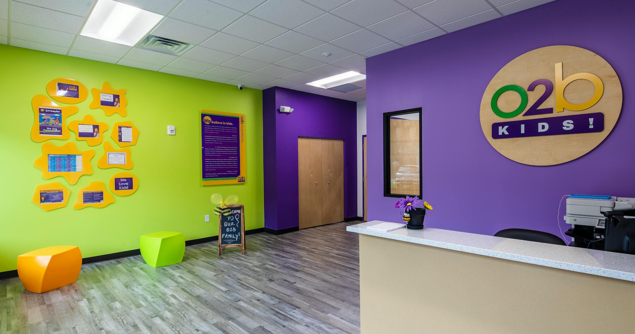 Reception area with purple and lime green walls, O2B Kids! logo on wall