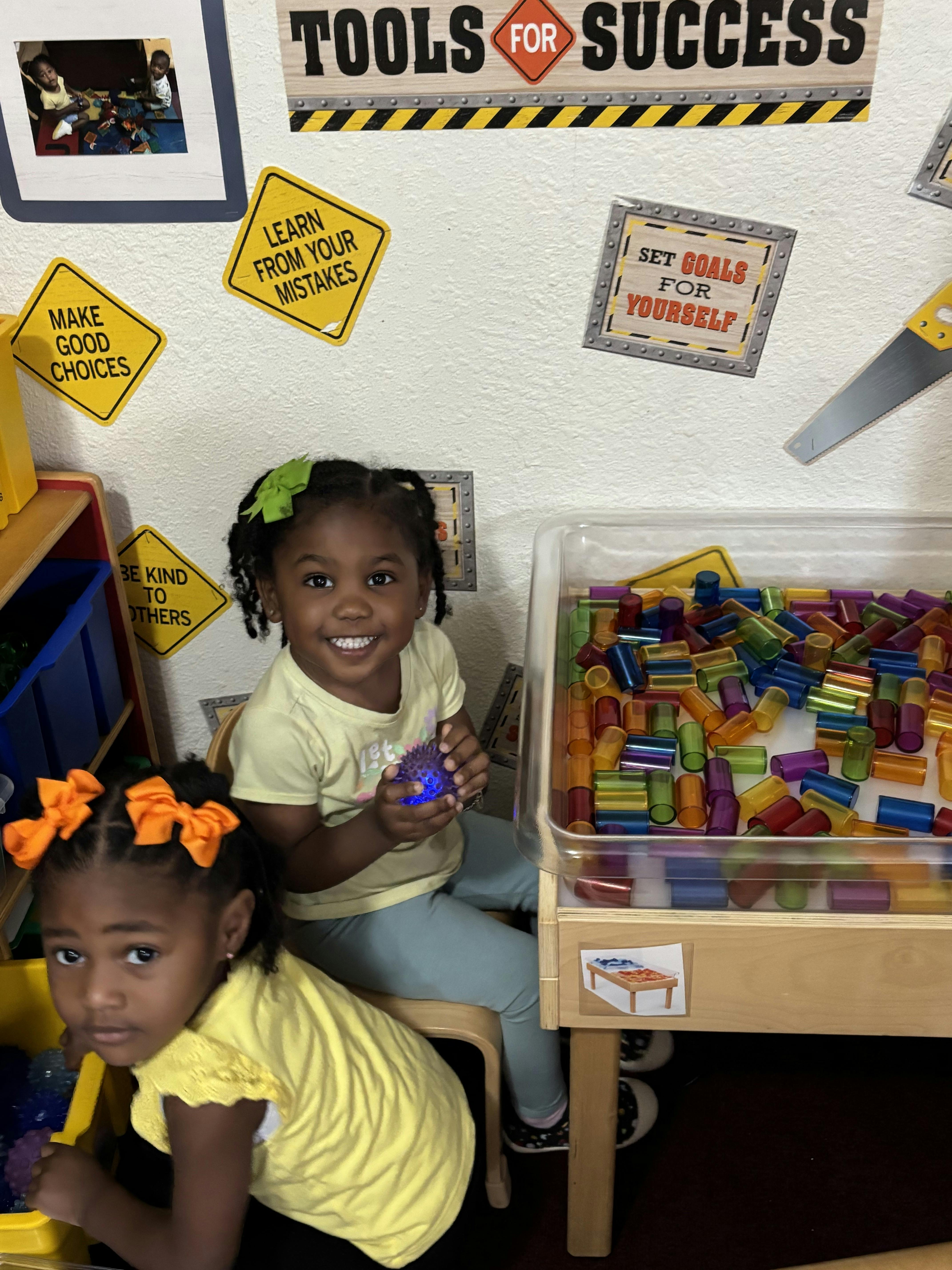 Two children playing with colorful cylinders at a classroom sensory table