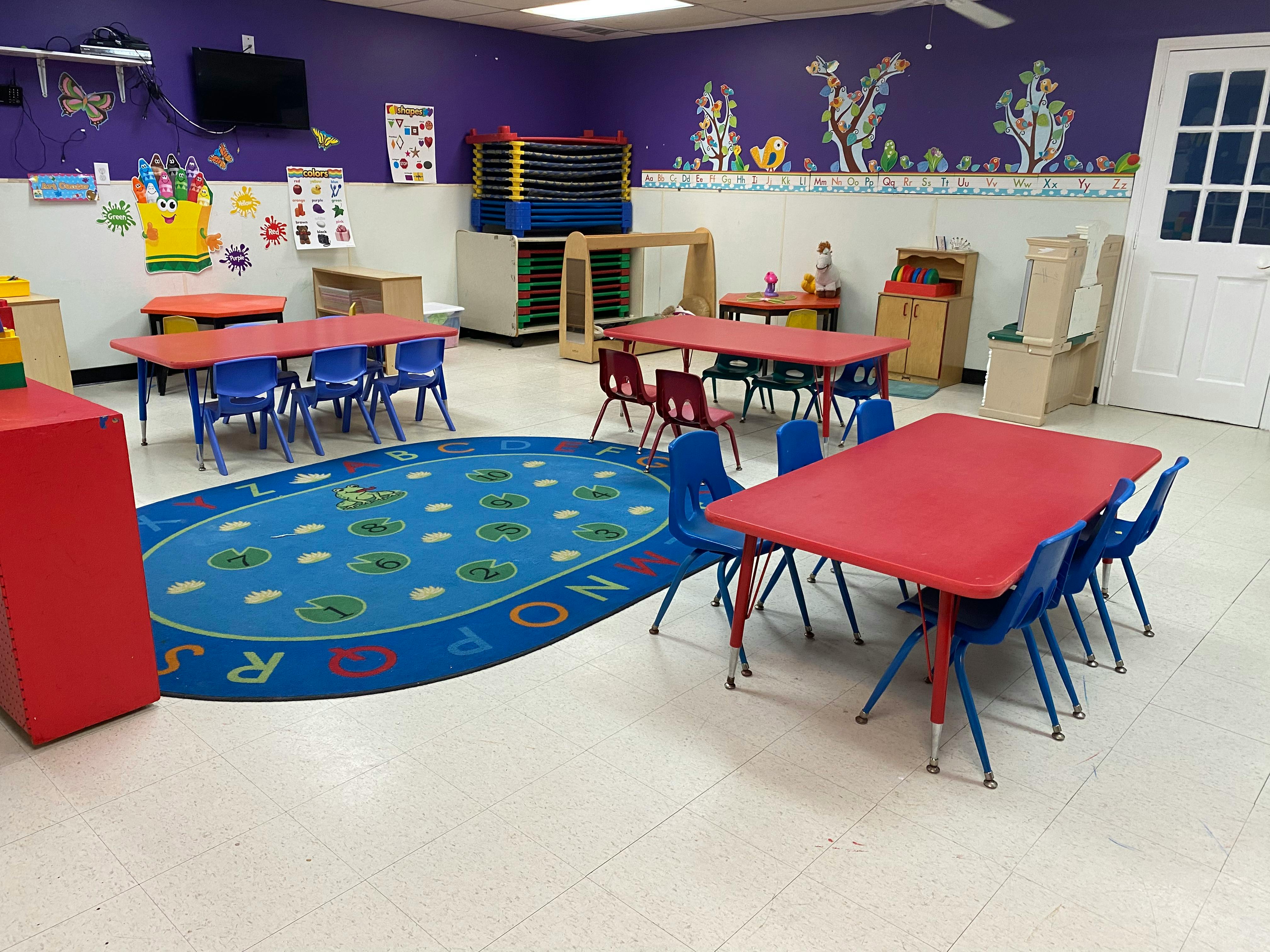 Classroom with red tables, blue chairs, and a blue oval rug