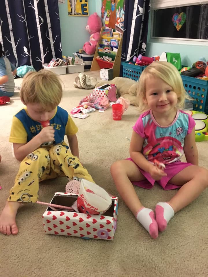 Two children sitting on the floor, one eating a popsicle and one smiling