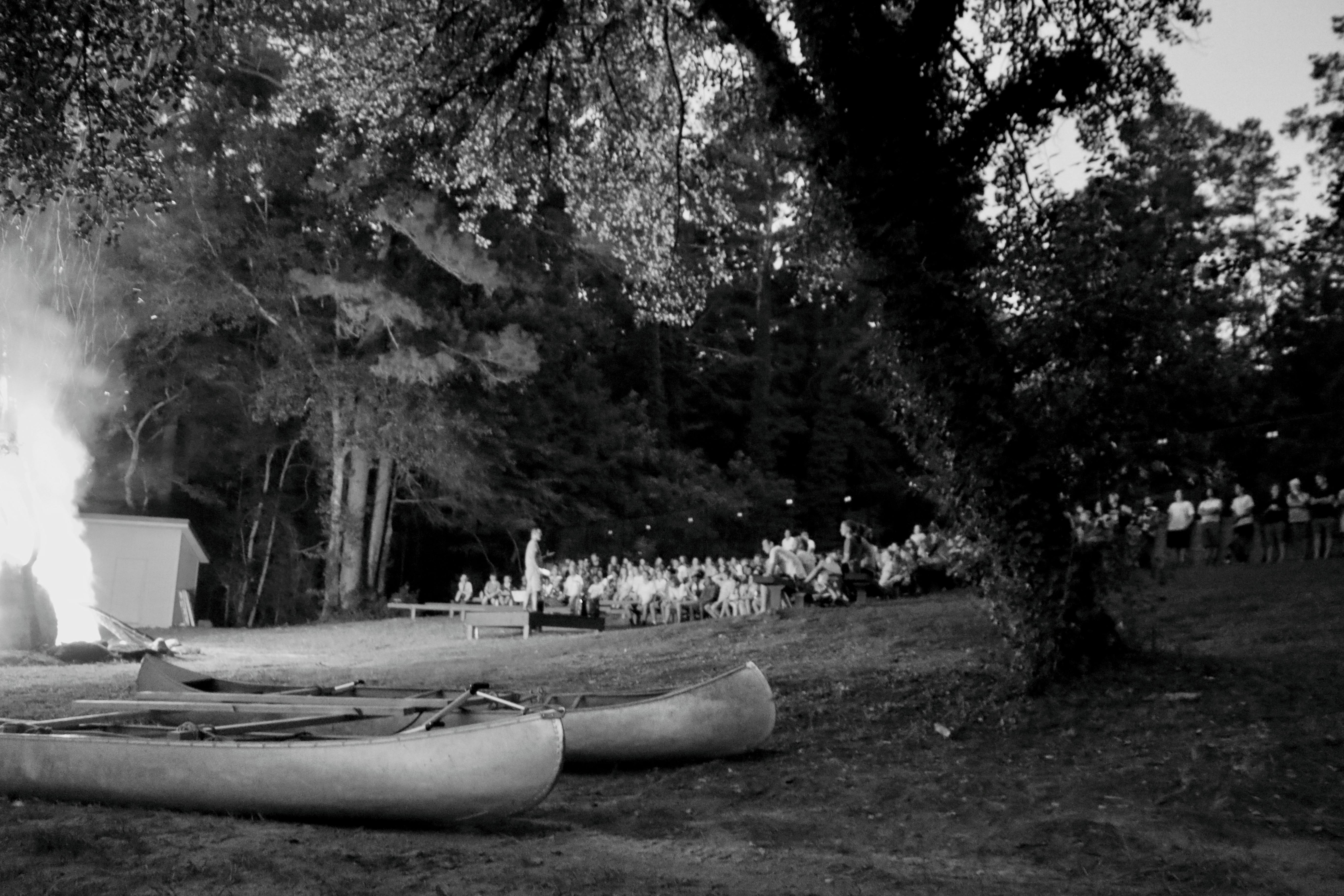 Two canoes on grass near a large bonfire and people gathered in the background