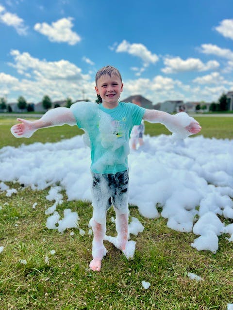 Child standing in grass covered in foam