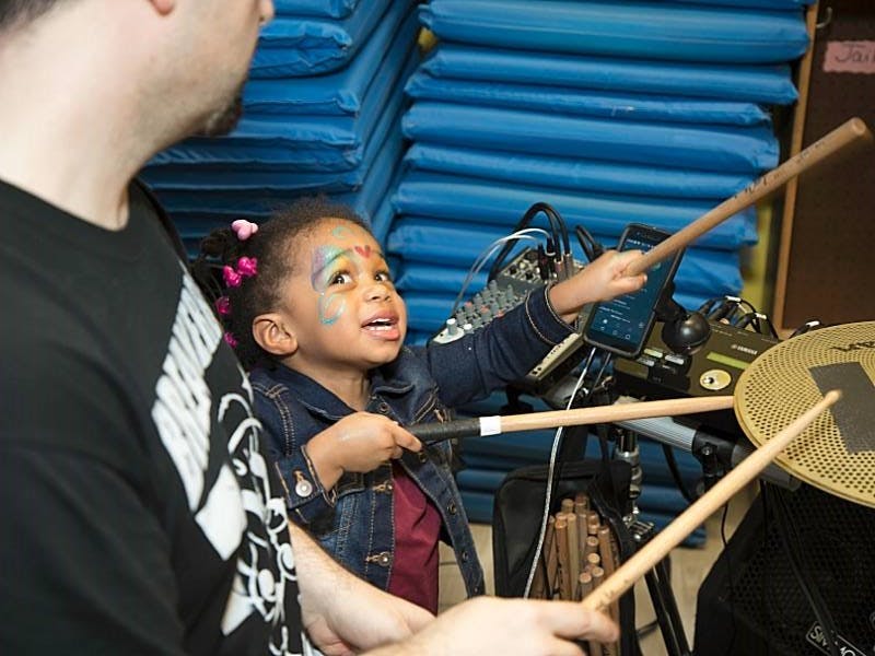 Child with face paint holding drumsticks with a person
