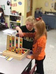 Two children playing with a wooden block game in a classroom