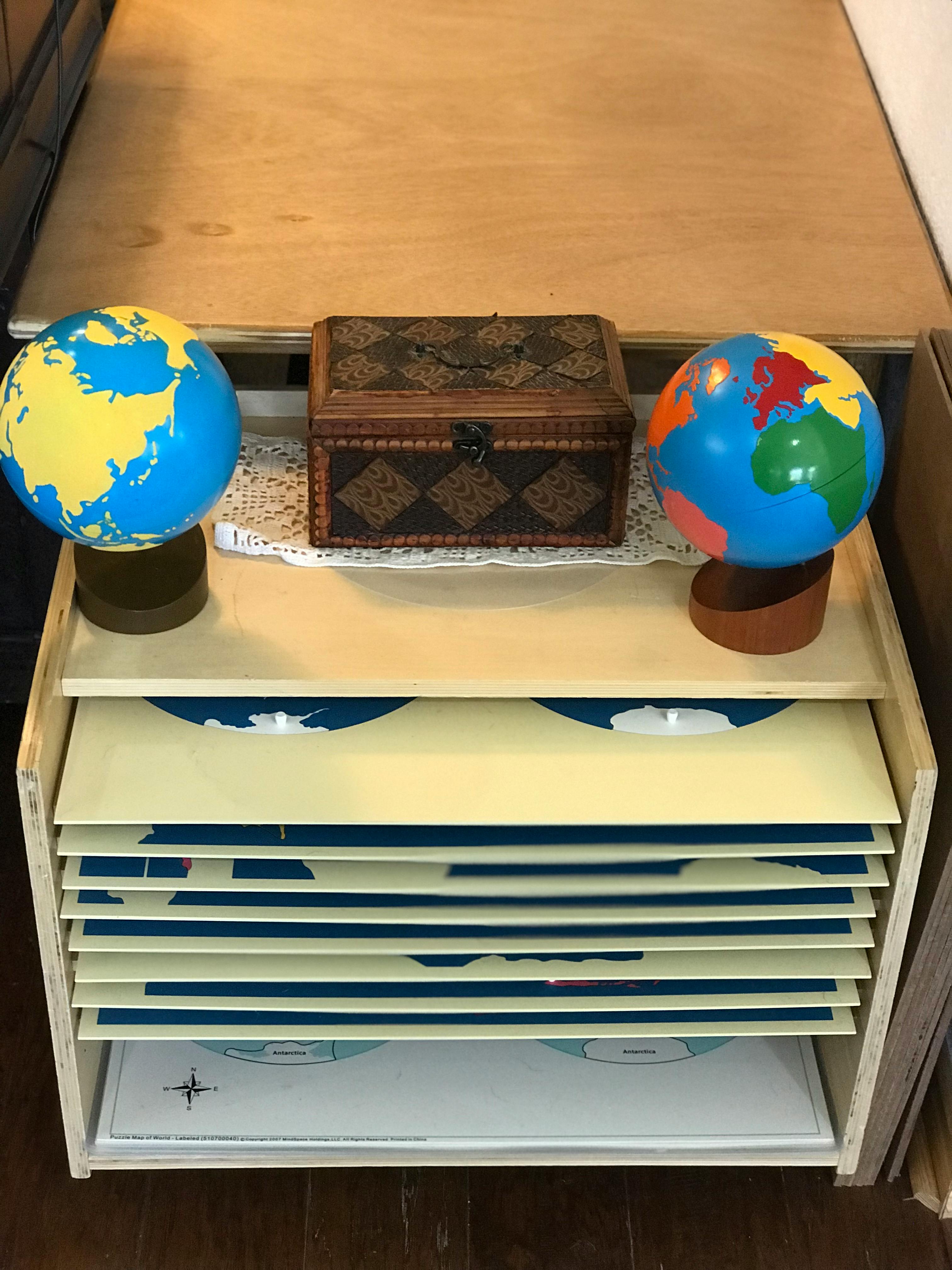 Two globes and a wooden box on a shelf with map puzzles