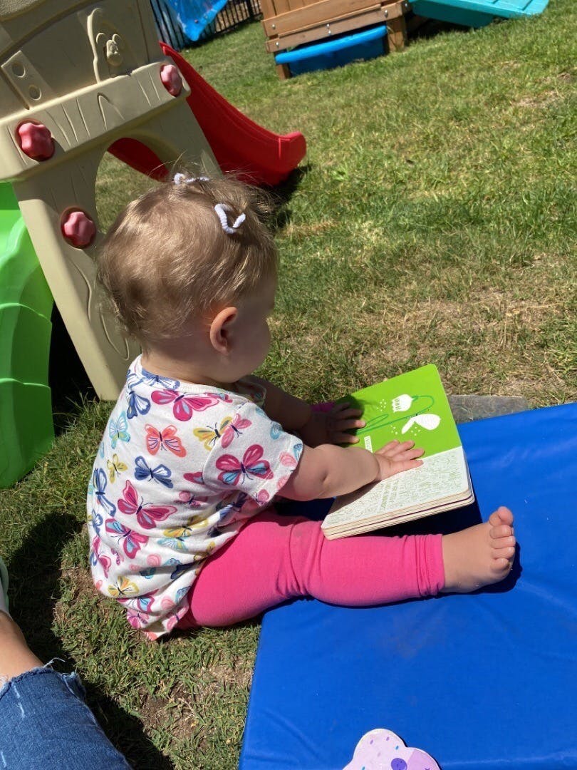 Child sitting on a blue mat reading a book outdoors