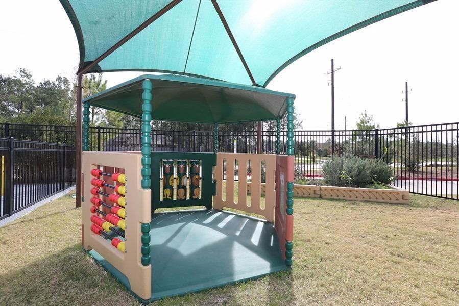 Play structure with a green shade canopy over a grassy area