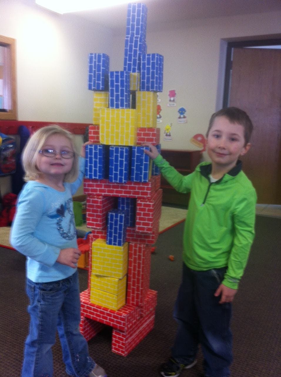 Two children standing next to a tall structure made of colorful blocks