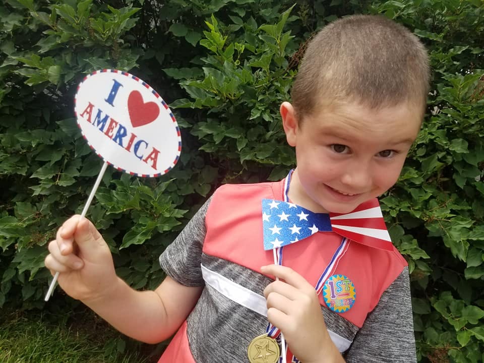Child holding "I love America" sign and American flag bow tie