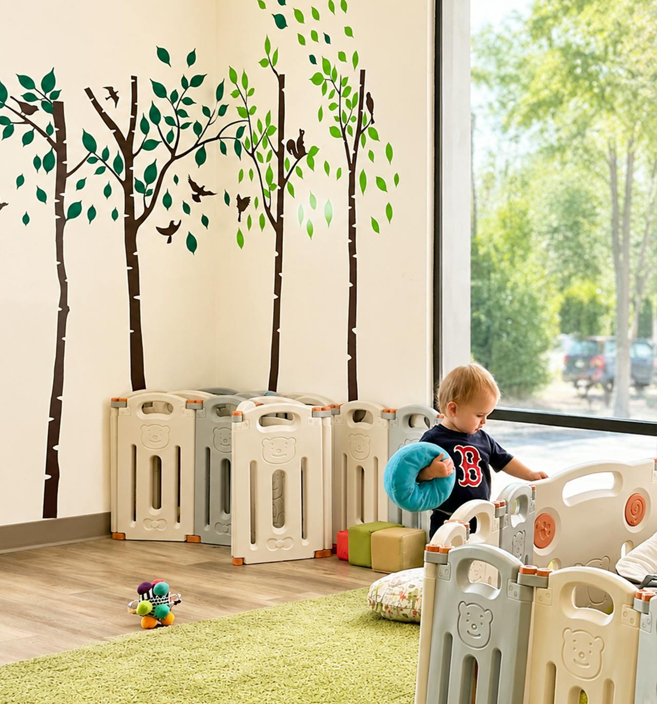 Child standing inside a playpen in a room with tree wall decals