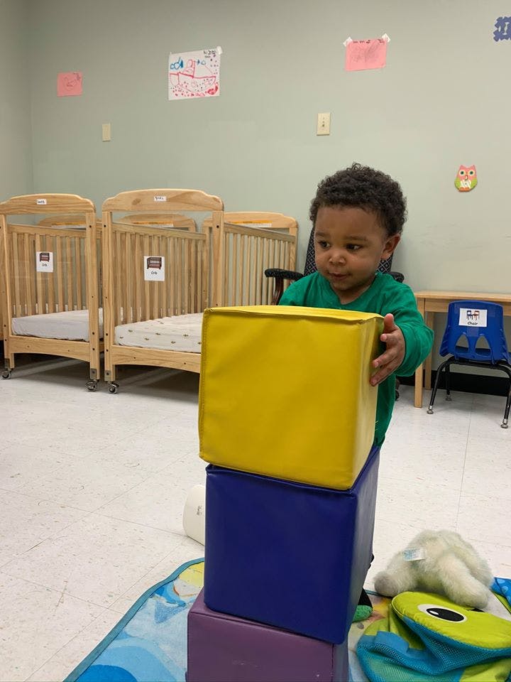 Child stacking large soft blocks in a room with cribs