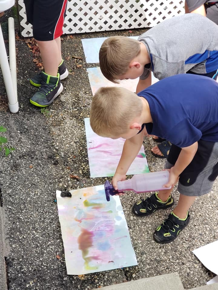 Two children spraying paint onto paper on the ground