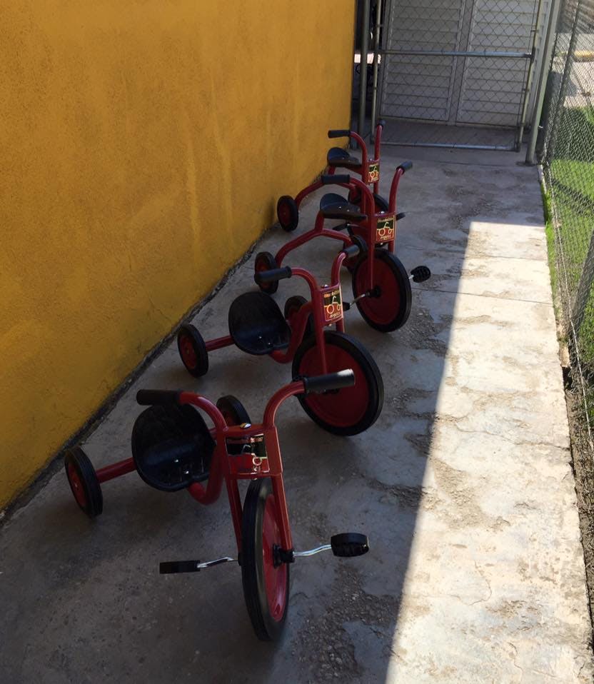 Three red tricycles lined up against a yellow wall