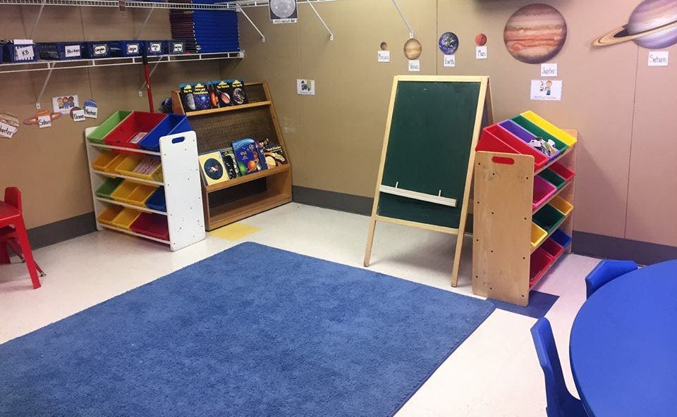 Classroom with blue rug, chalkboard, and toy shelves