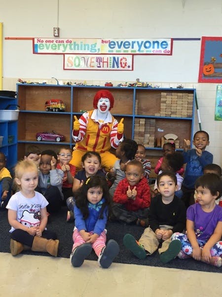 Clown sitting on a shelf with children sitting on the floor in a classroom