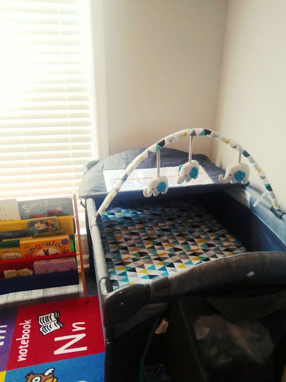 Playard with a mobile and a patterned mattress next to a bookshelf and alphabet rug