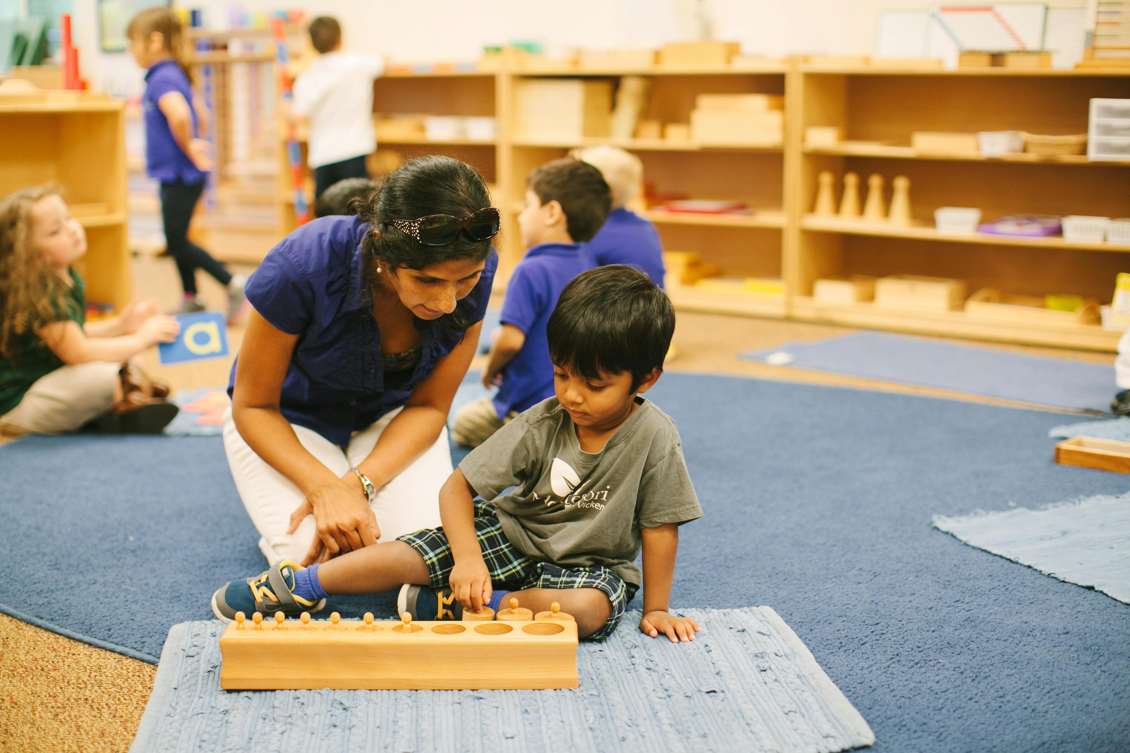 Adult and child on floor playing with wooden blocks in a classroom