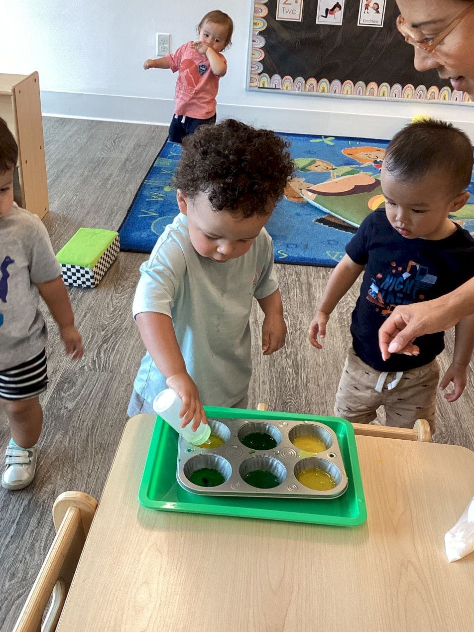 Child pouring liquid into a muffin tin with other children nearby