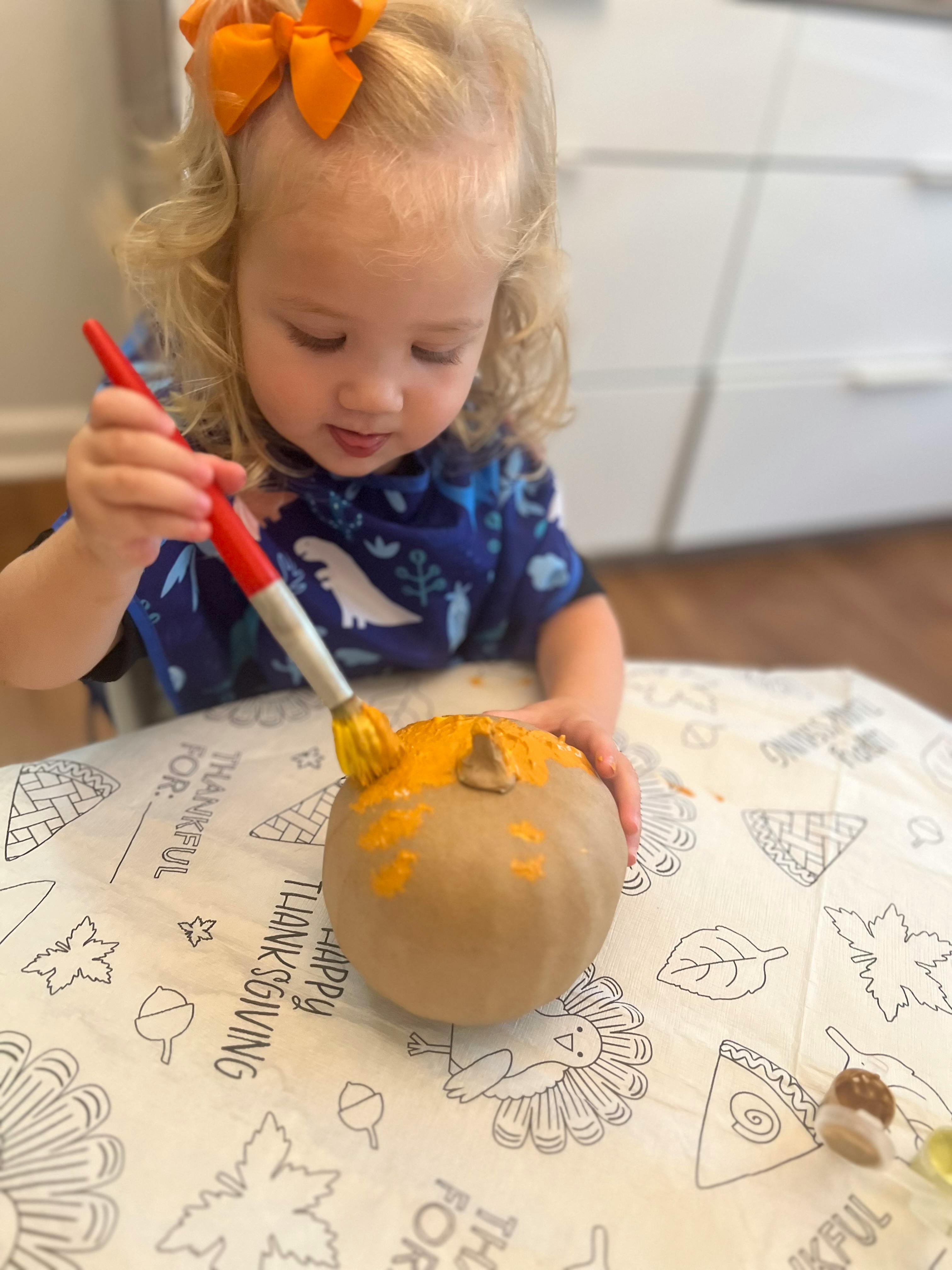 Child painting a small pumpkin with a brush