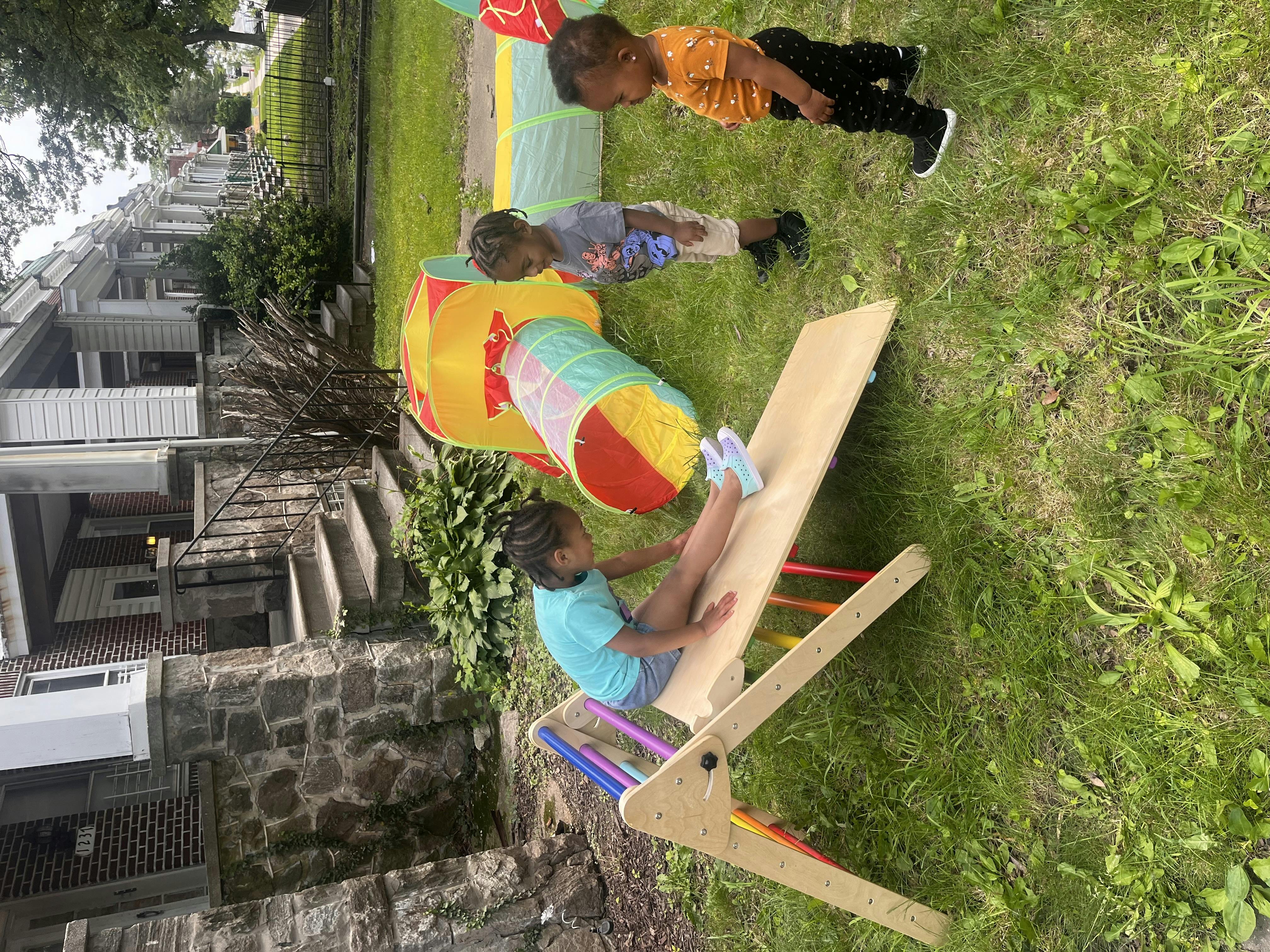 Three children playing on a seesaw and in a tunnel on a grassy area