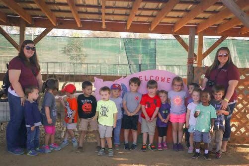 Two adults with a group of children standing in front of a pink pig statue