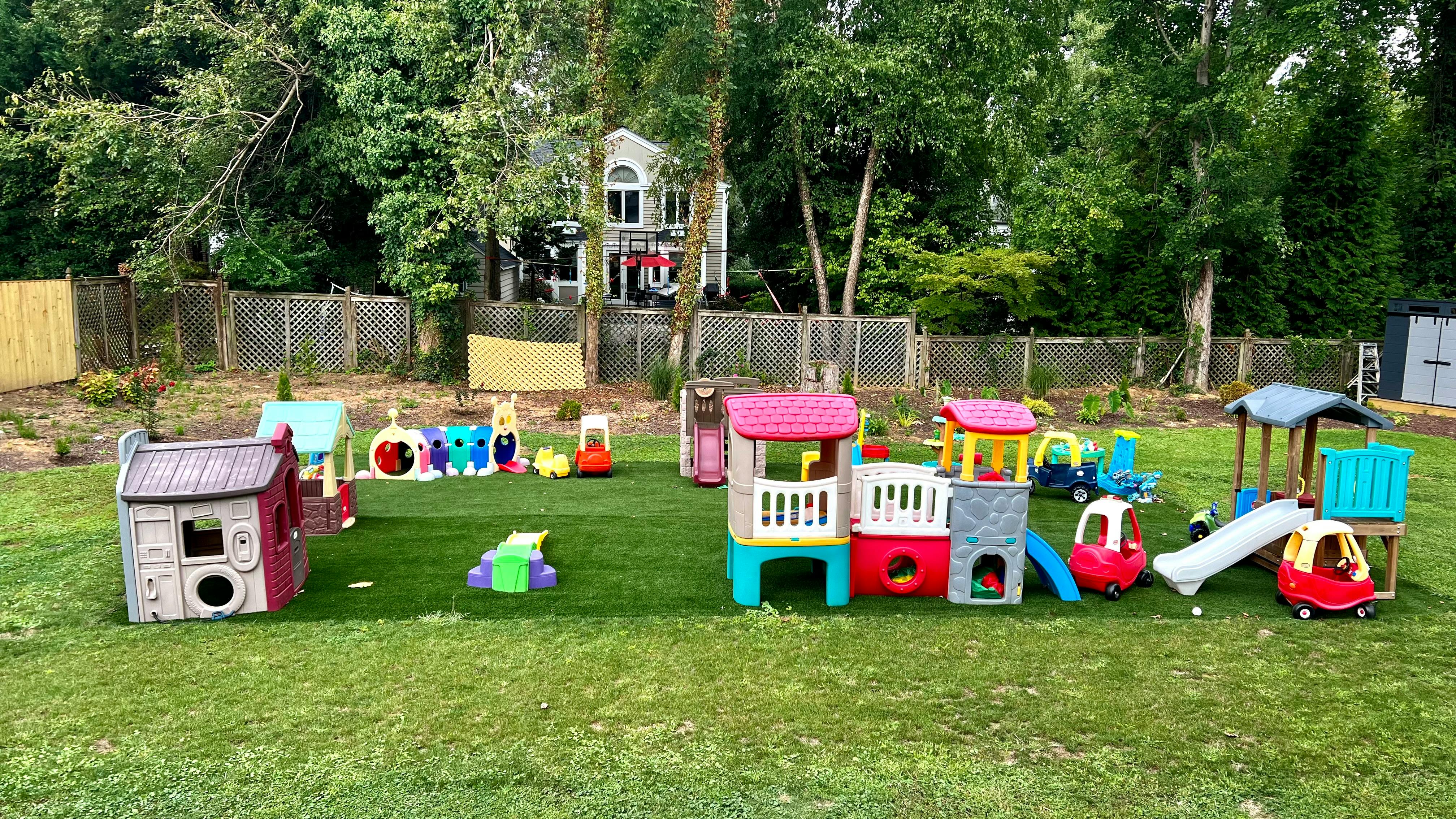 Outdoor play area with multiple colorful playhouses, slides, and ride-on toys