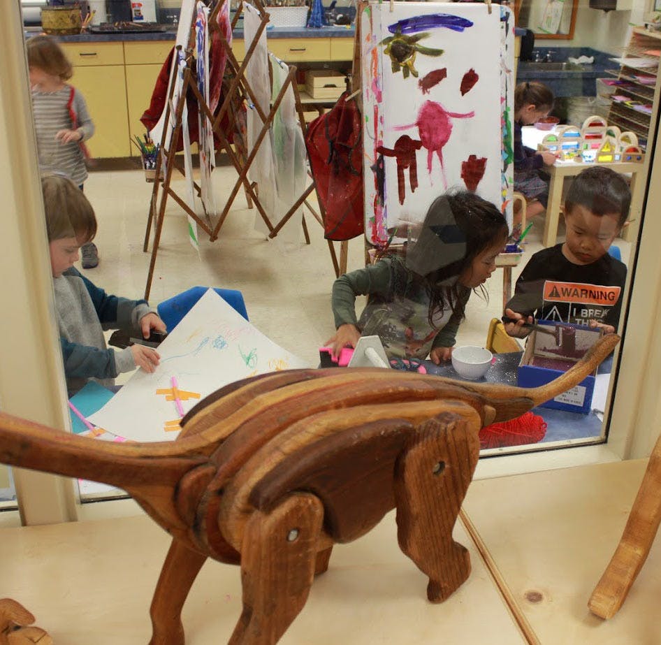 Children in a classroom with a wooden dinosaur toy in the foreground