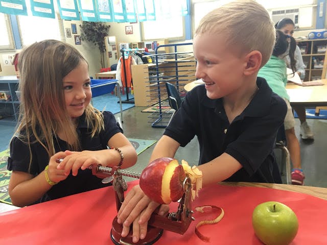 Two children peeling an apple with a peeler in a classroom
