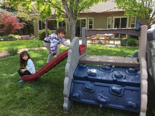 Two children playing on a slide and climbing structure in a yard