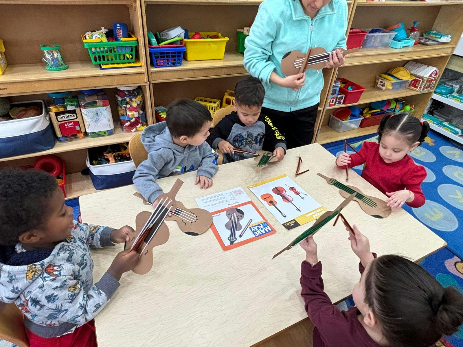 Adult and children making string instruments from cardboard in a classroom