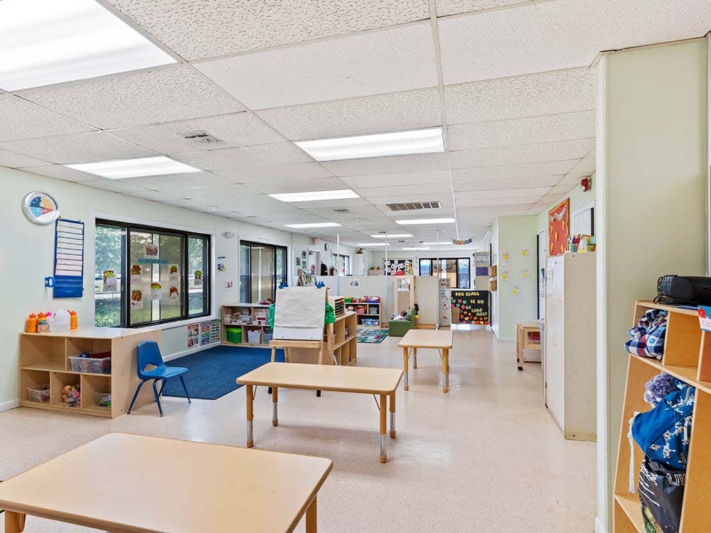 Empty classroom with small tables and chairs, large windows, and shelves