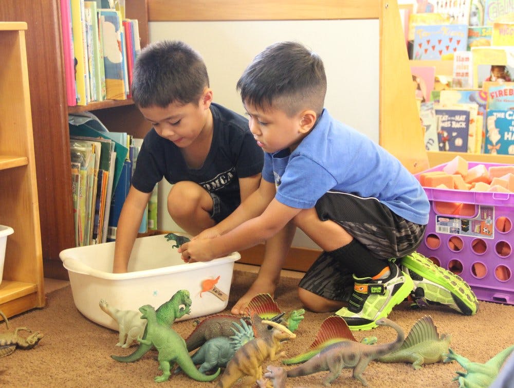 Two children playing with dinosaur toys and a white tub on the floor