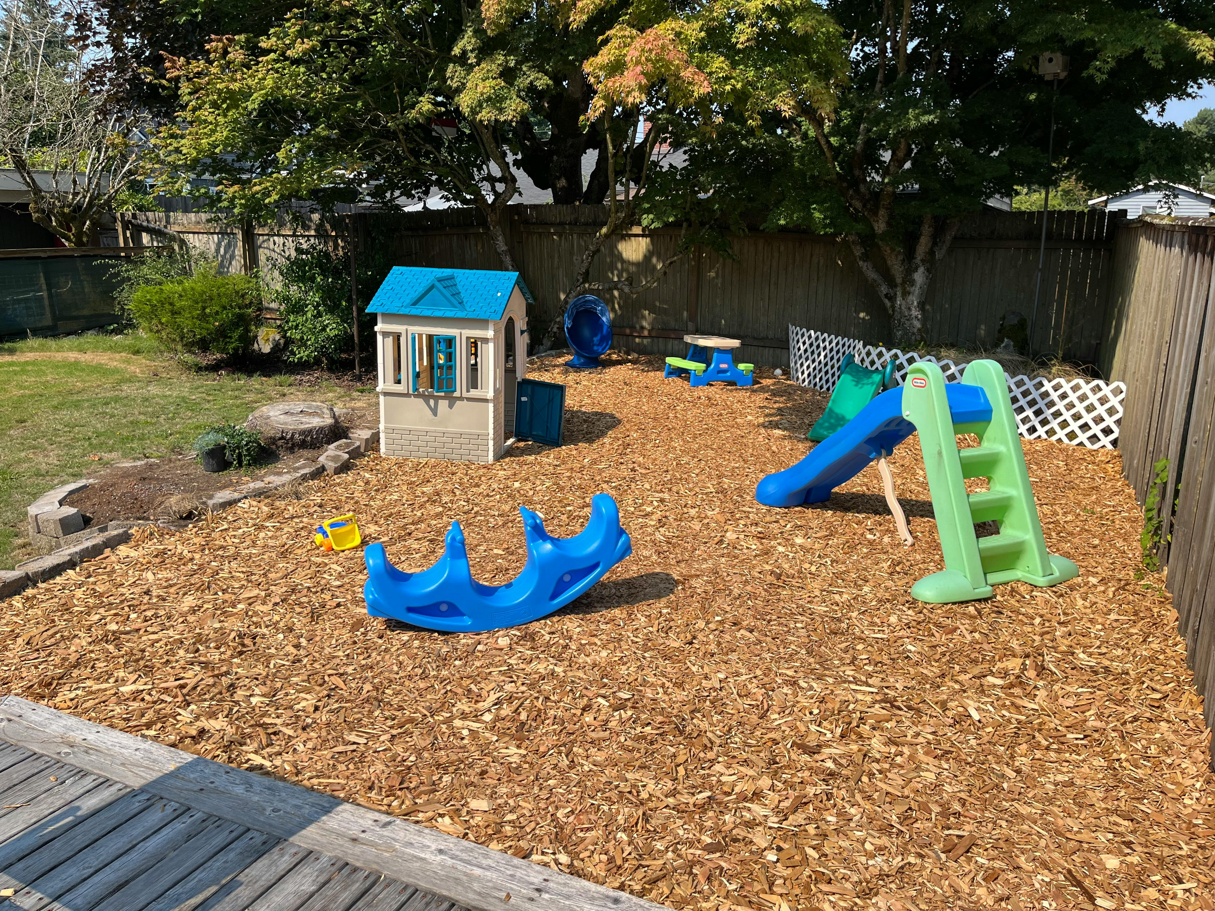 Playground with wood chips, playhouse, blue seesaw, and green and blue slide