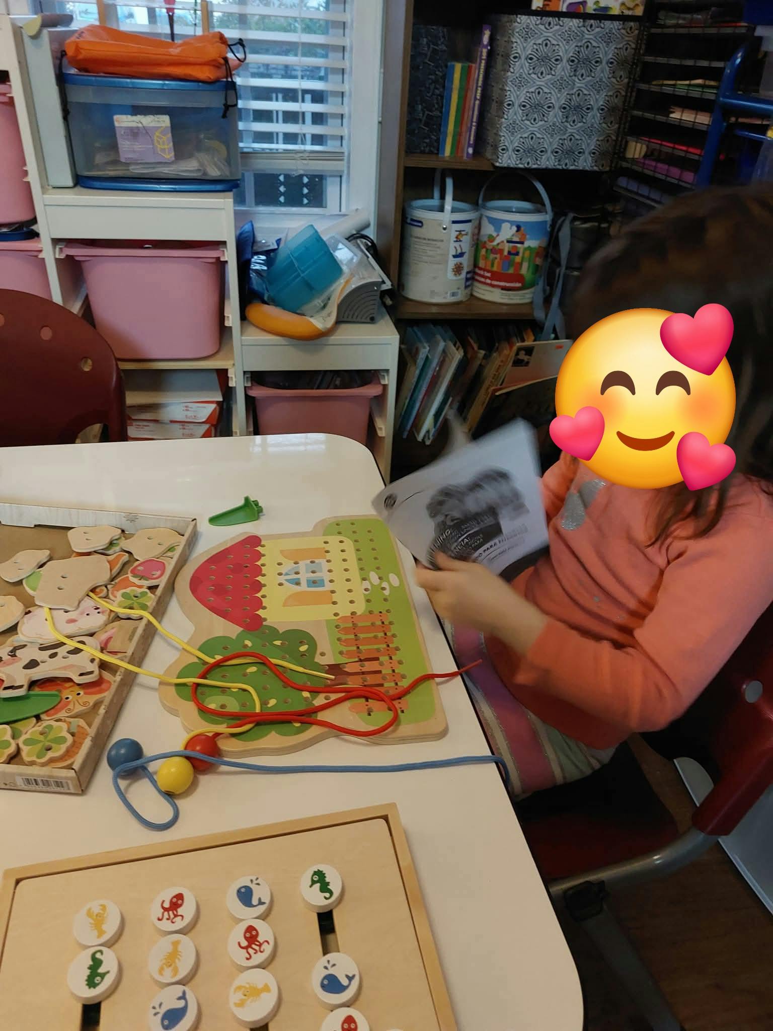 Child looking at a paper in a playroom with lacing toys on a table