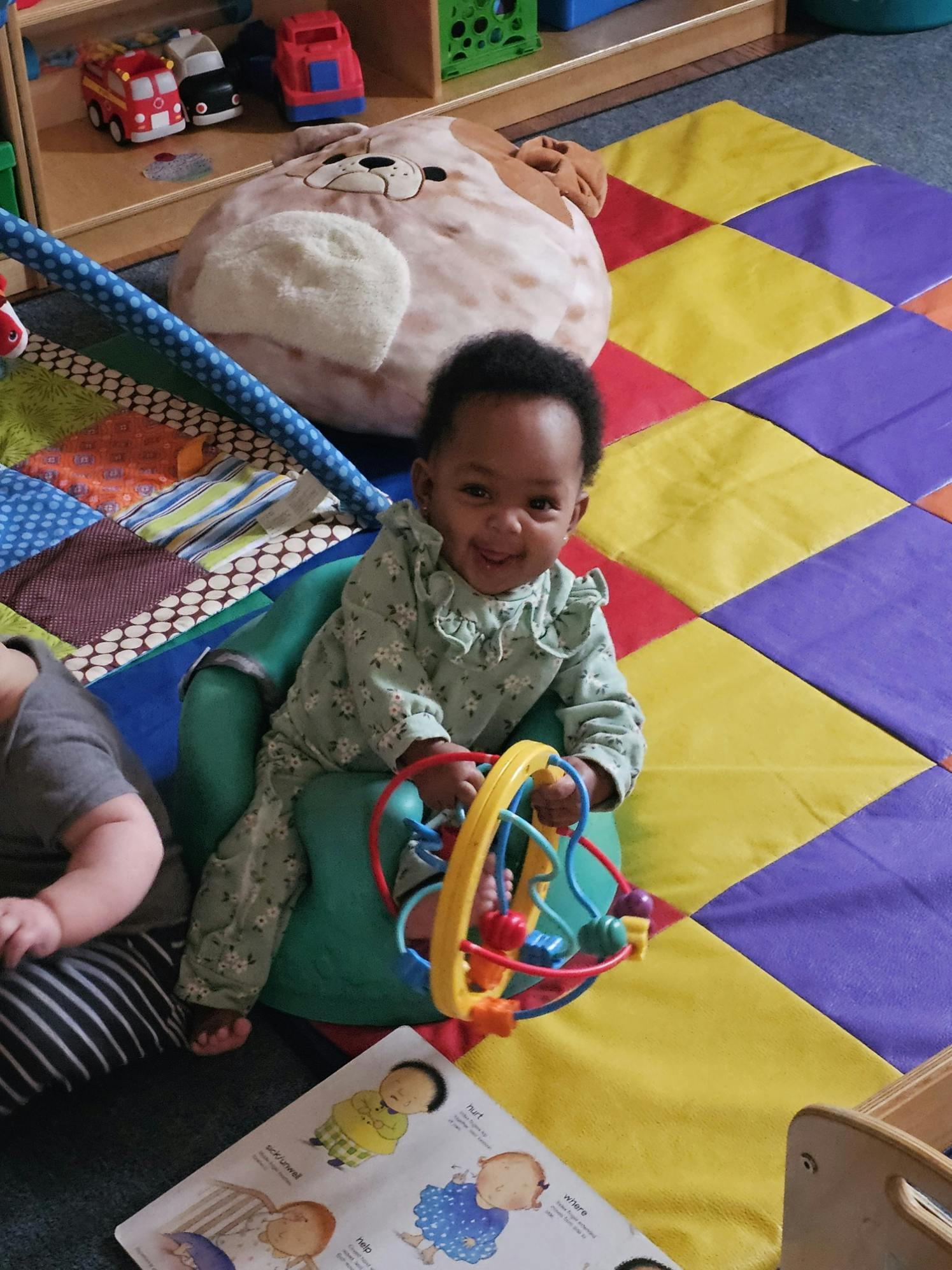 Child sitting in a green chair holding a colorful toy