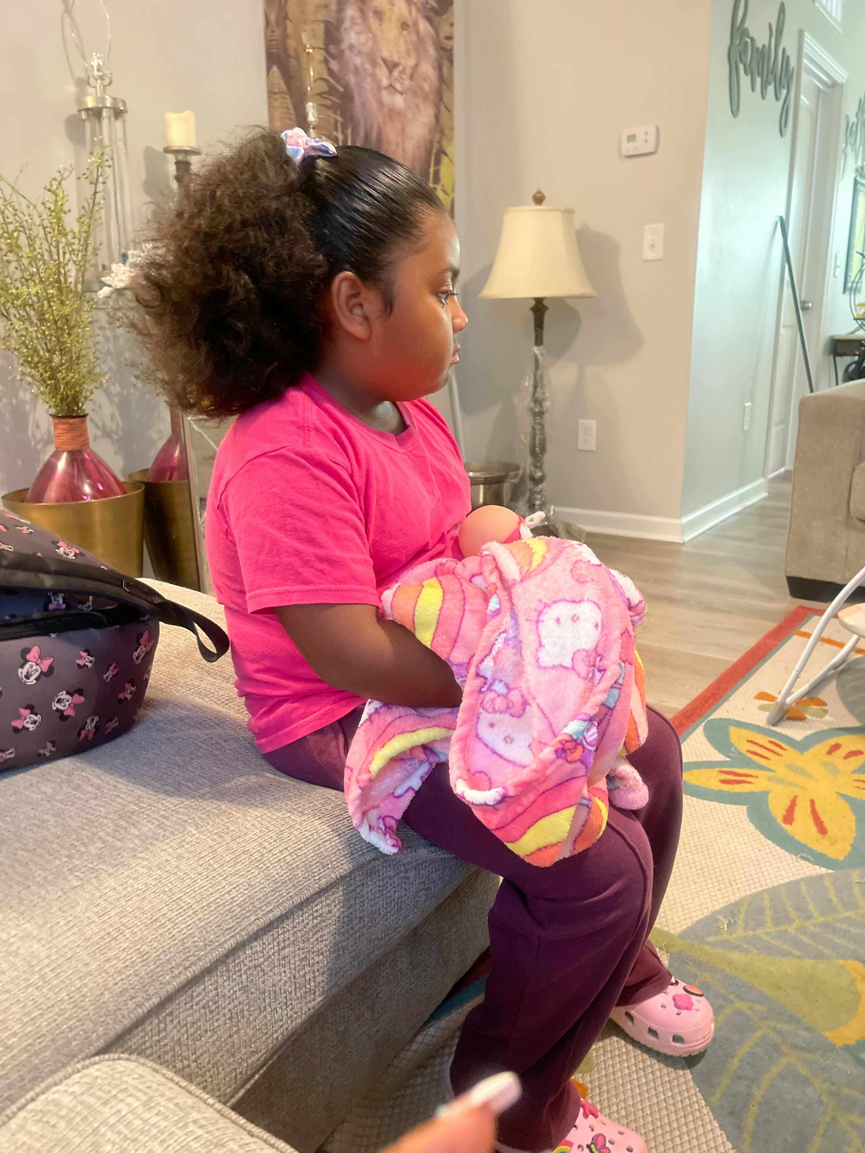 Child sitting on a couch holding a doll wrapped doll