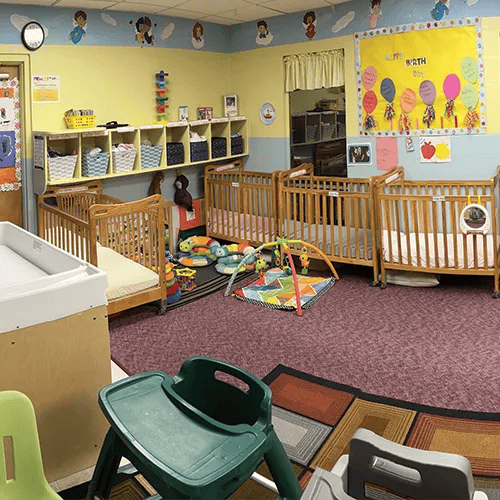 Nursery room with multiple cribs, play mats, and a changing table