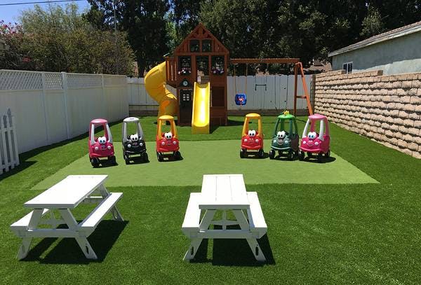 Playground with play structure, toy cars, and picnic tables on artificial turf