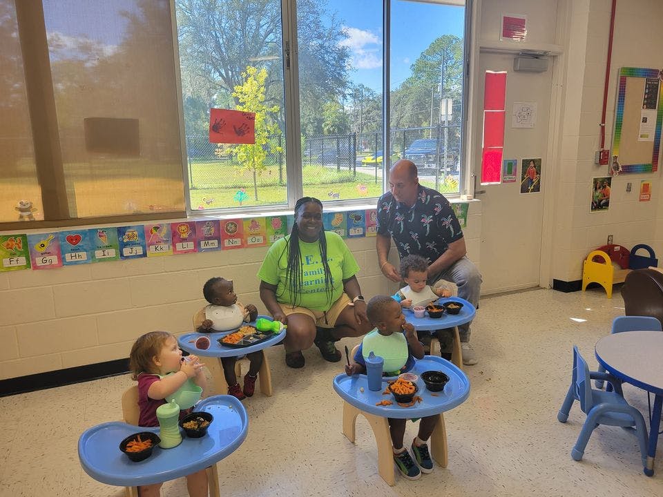 Two adults with several children in high chairs in a classroom