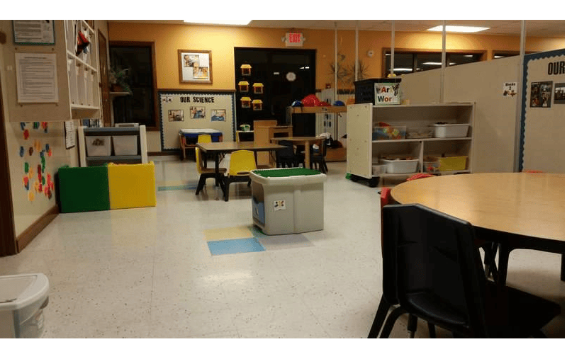 Empty classroom with small tables and chairs, shelves, and a bulletin board that says "Our Science"