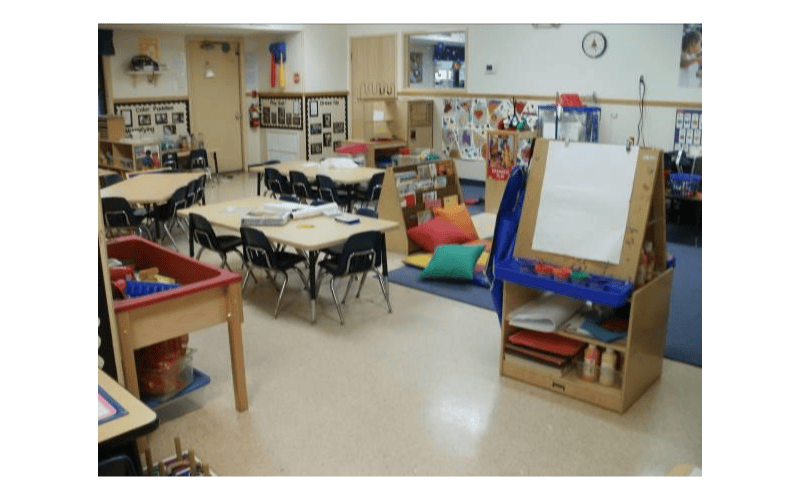An empty early childhood classroom with small tables and chairs